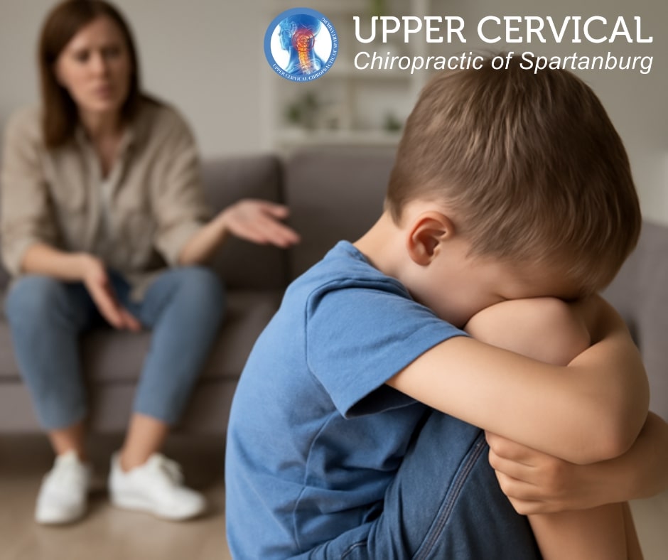 Child covering face at desk beside educational graphic about neurodeflective behaviors including learning difficulties, emotional dysregulation, and social challenges.